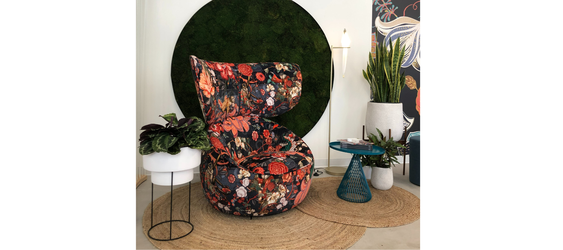 an oversized lounge chair with a red upholstery with animals on it, a moss wall behind and a standing lamp shaped like a bird
